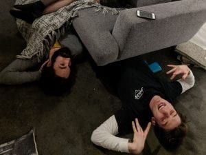Two people lying on the floor underneath a couch.